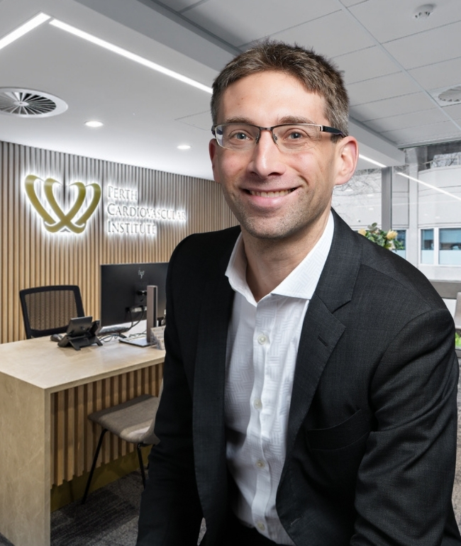 Image of Dr Jonathan Lipton infront of the reception desk with PCI sign behind. Relaxed pose.
